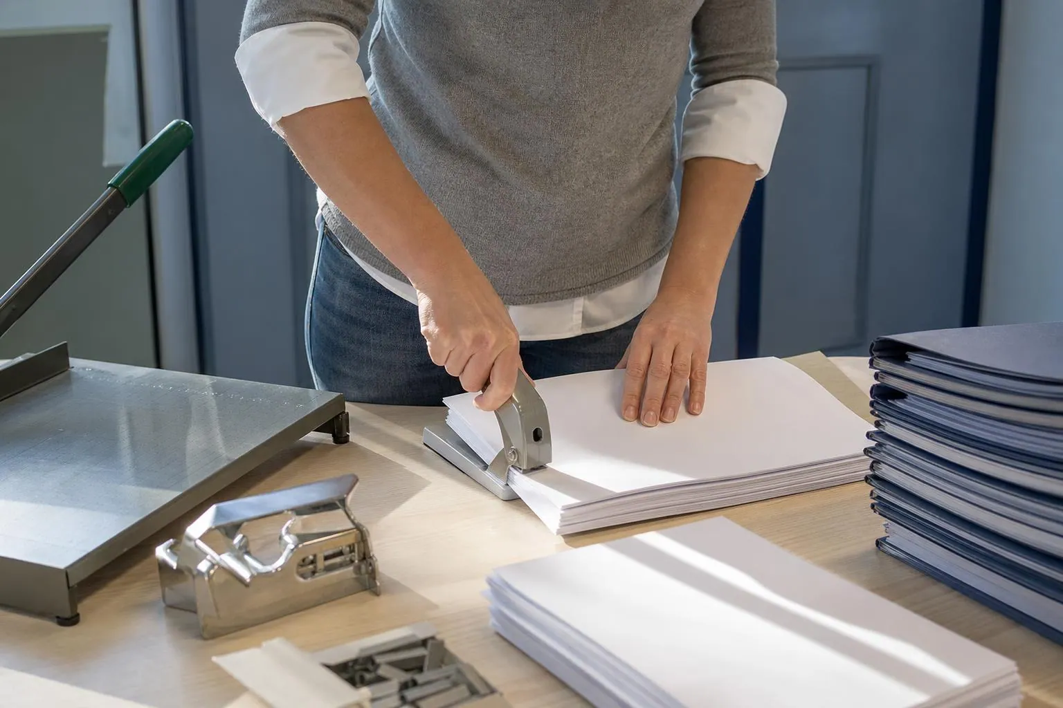 Agente administrative agrafant des jeux de documents alignés sur une table de secrétariat avant une séance